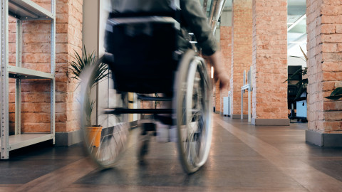 Een persoon in een rolstoel beweegt zich door de gang van een gebouw.