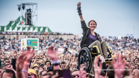 Een jonge vrouw crowdsurfing in rolstoel tijdens een optreden in de buitenlucht; foto Hans Peter van Velthoven