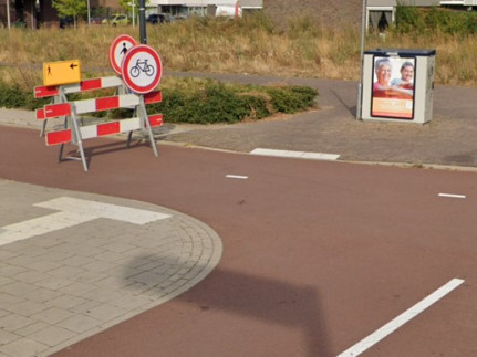 Een onveilige en onoverzichtelijke verkeerssituatie voor voetgangers met obstakels zoals een verkeersbord op het fietspad en een elektriciteitskast op de stoep aan het einde van de geleidelijnen.