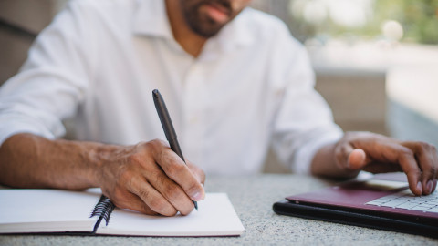 man met pen, schrijfblok en laptop