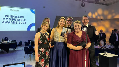 Twee mannen en drie vrouwen in feestkleding staan met een award op het podium van de Computable Awards 2024