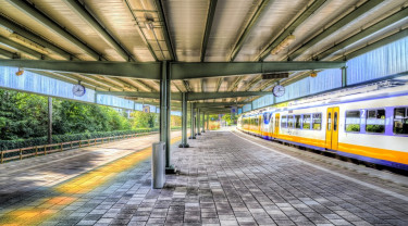 een leeg perron op een treinstation. er rijdt een sprinter voorbij.