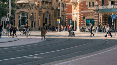 kruispunt in Amsterdam waarop je een tramlijn, fietspad, weg en weggebruikers afbeeld ziet