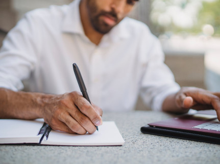 man met pen, schrijfblok en laptop